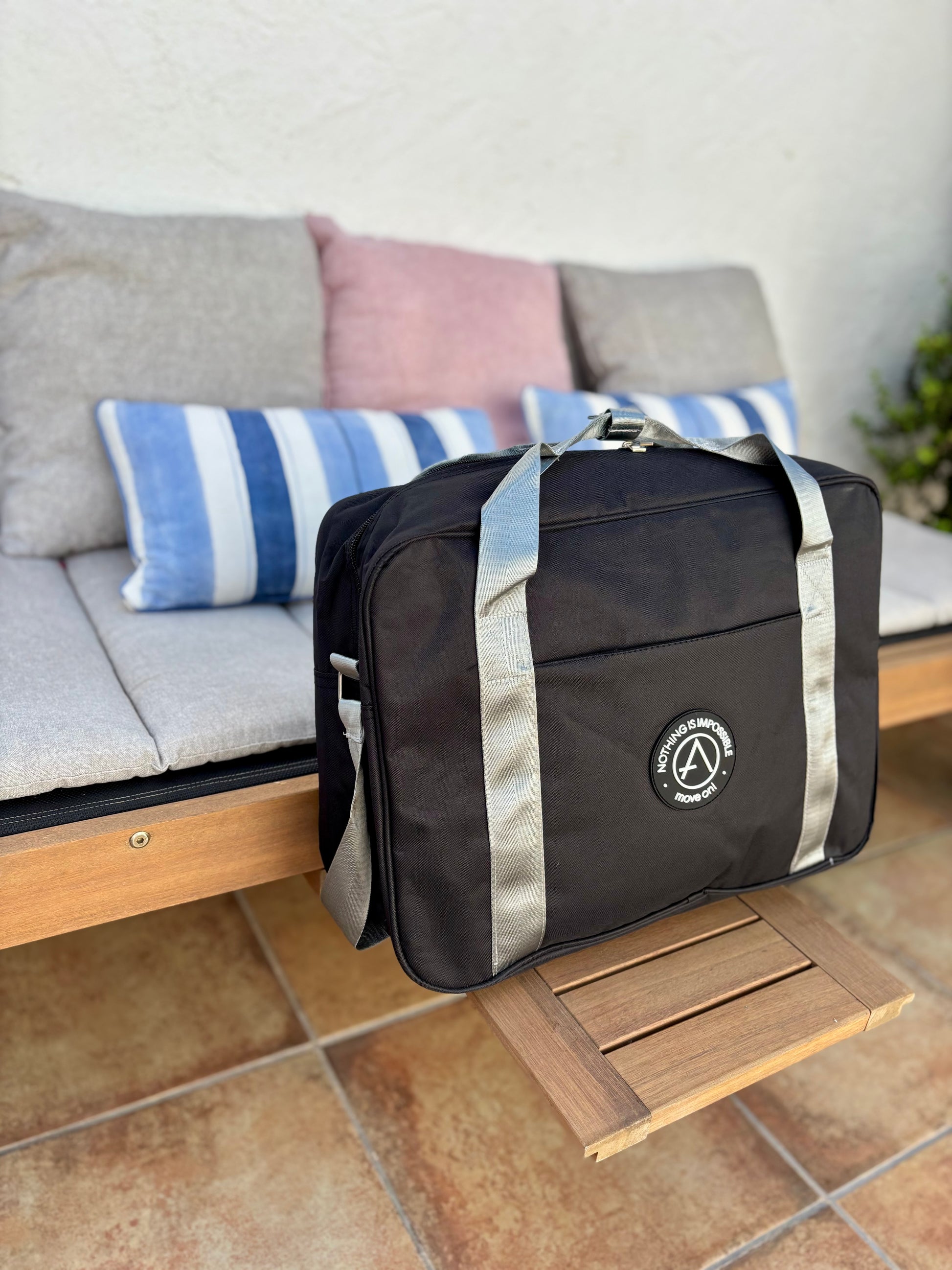 Bolsa de viaje negra rectangular con logo motivacional frontal y asas en color gris claro