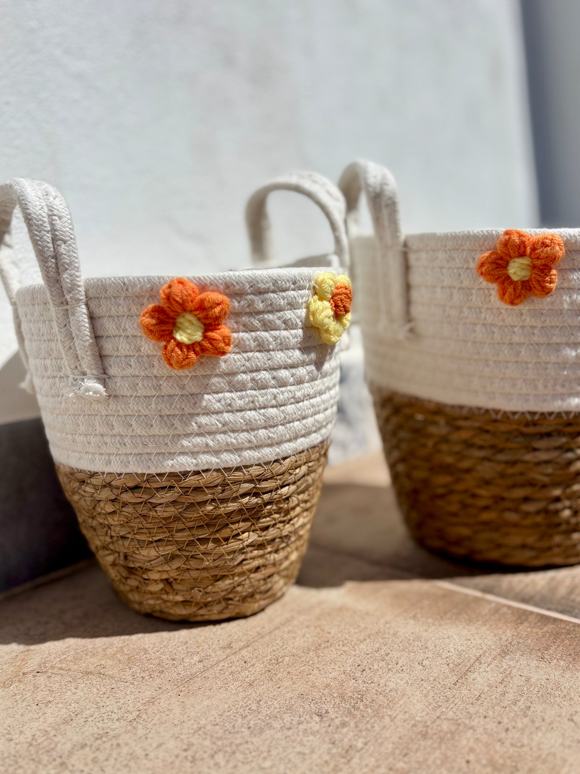 Detalle de flores de algodón en tonos naranja y amarillo sobre cesto de mimbre y algodón blanco