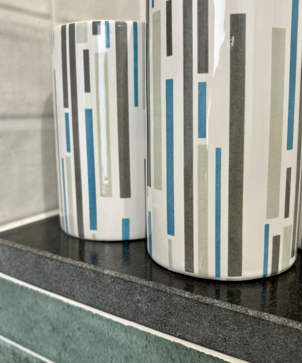 Primer plano de set de baño con textura cerámica blanca, rayas grises y azules y dispensador en acabado cromado brillante