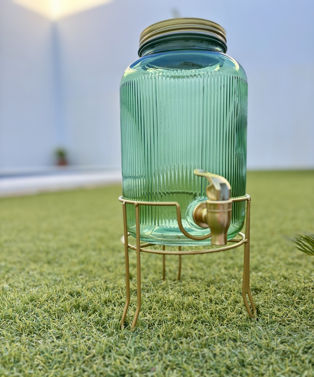 Dispensador de bebidas de vidrio estriado color verde esmeralda con detalles dorados, accesorio elegante para mesa, jardín o terraza