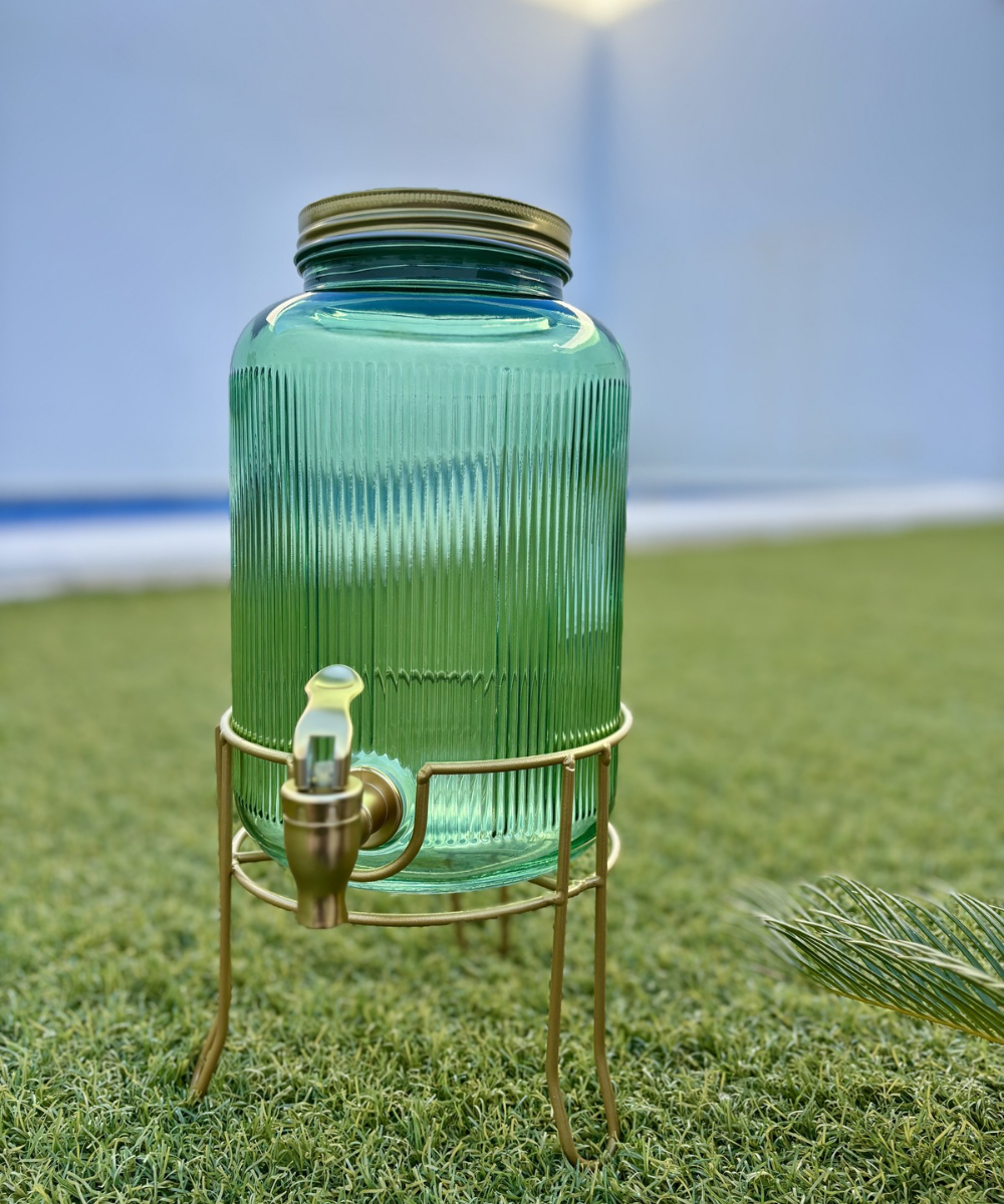 Dispensador de bebidas Emerald Gold de vidrio verde esmeralda con soporte dorado, ideal para servir limonada, agua o zumos en reuniones y eventos