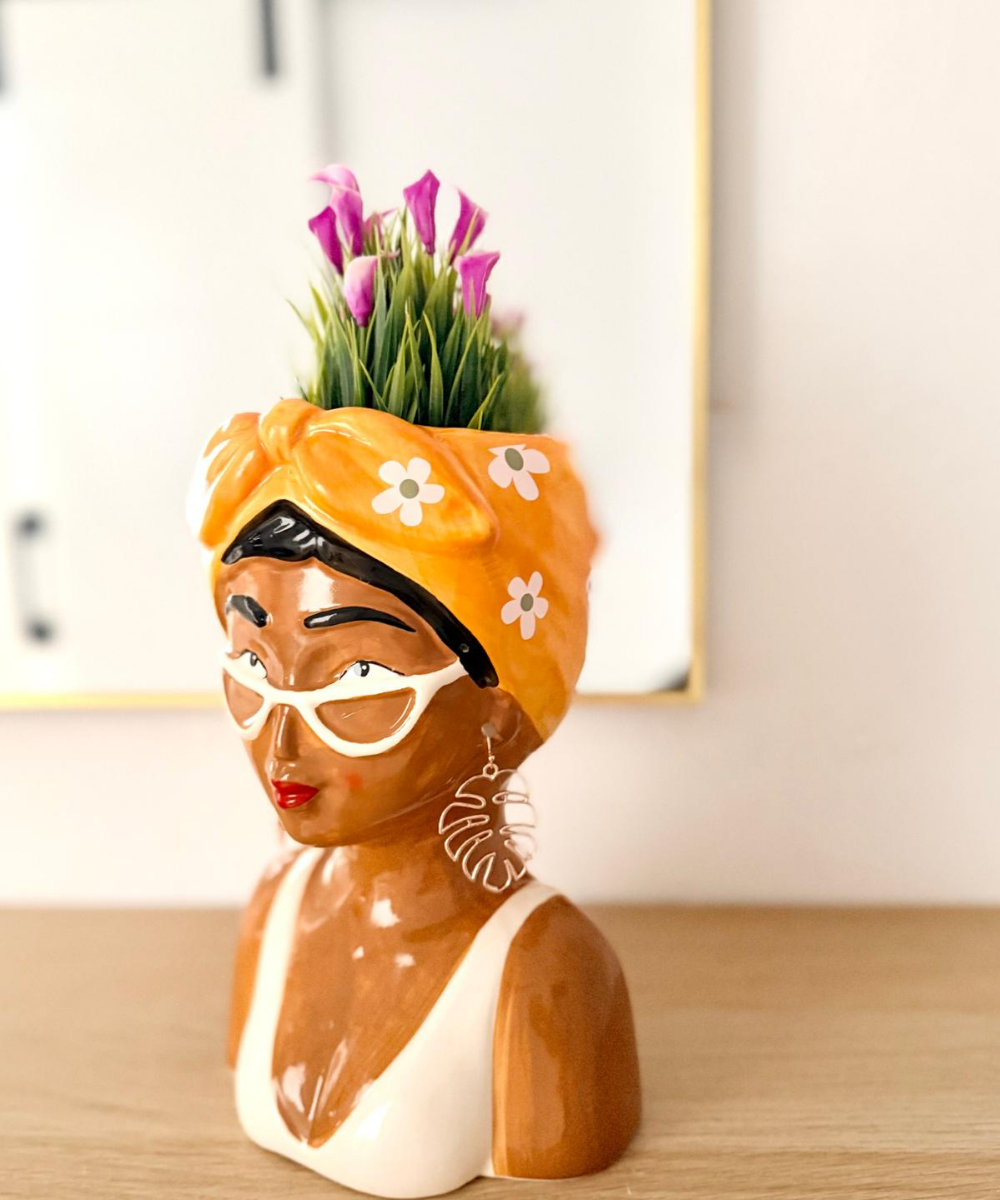 Jarrón decorativo Frida Pop morena con pañuelo naranja, gafas blancas y pendientes de hoja de palmera, ideal para decorar cualquier rincón. 