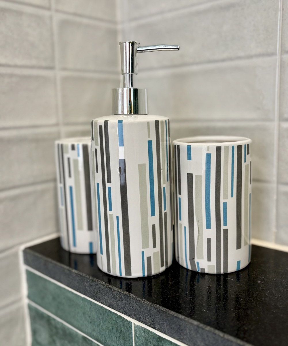 Accesorios de baño redondos en cerámica blanca con rayas decorativas grises y azules y dispensador cromado vertical
