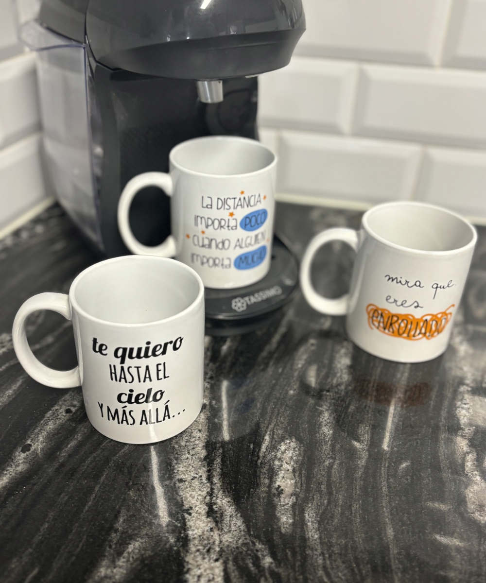 Tres tazas con frases diferentes vistas desde un ángulo superior, colocadas en una cocina alrededor de una cafetera.